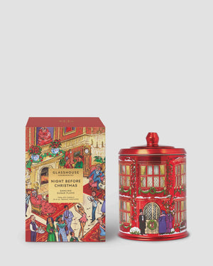 A Christmas-themed glass jar candle and its matching retail box by Glasshouse, featuring a festive red building illustration with holiday figures.