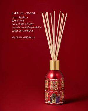 A red reed diffuser bottle with laser-cut holiday window detailing and natural reed sticks