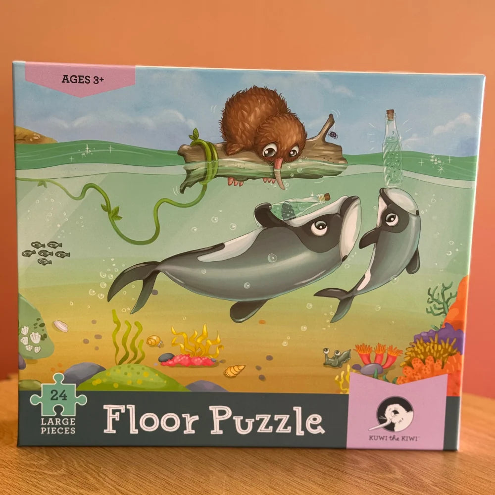 Puzzle - Māui Dolphin Mischief - 24 piece A boxed children's floor puzzle by Lakes Pieces featuring an underwater illustration of two dolphins, a brown rodent on a log, and colorful coral.