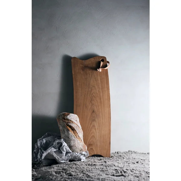 MUUBS Lyon Cutting Board - Natural A long, narrow wooden serving board with a natural live edge and a small leather hanging loop A wooden cutting board with a leather handle