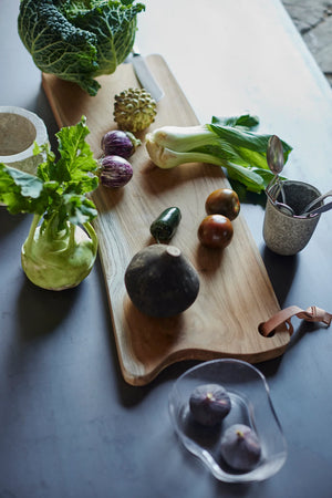 MUUBS Lyon Cutting Board - Natural A long, narrow wooden serving board with a natural live edge and a small leather hanging loop A wooden cutting board with a leather handle