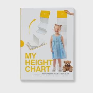 Suck UK My Height Chart A children's collapsible height chart book shown standing upright on a light gray background. The cover is white with bold yellow text reading 'MY HEIGHT CHART,' plus illustrations of folded pages and a young girl in a light blue dress standing beside the chart area.