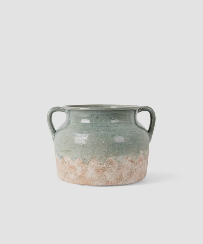 French Country Collections Varese Vessel Wide Pale Blue A rustic ceramic vase with two side handles, featuring a textured glaze that transitions from a muted sage green at the top to a distressed, earthy beige at the bottom