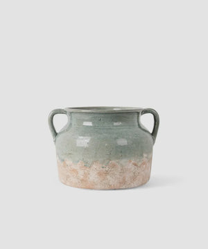 French Country Collections Varese Vessel Wide Pale Blue A rustic ceramic vase with two side handles, featuring a textured glaze that transitions from a muted sage green at the top to a distressed, earthy beige at the bottom