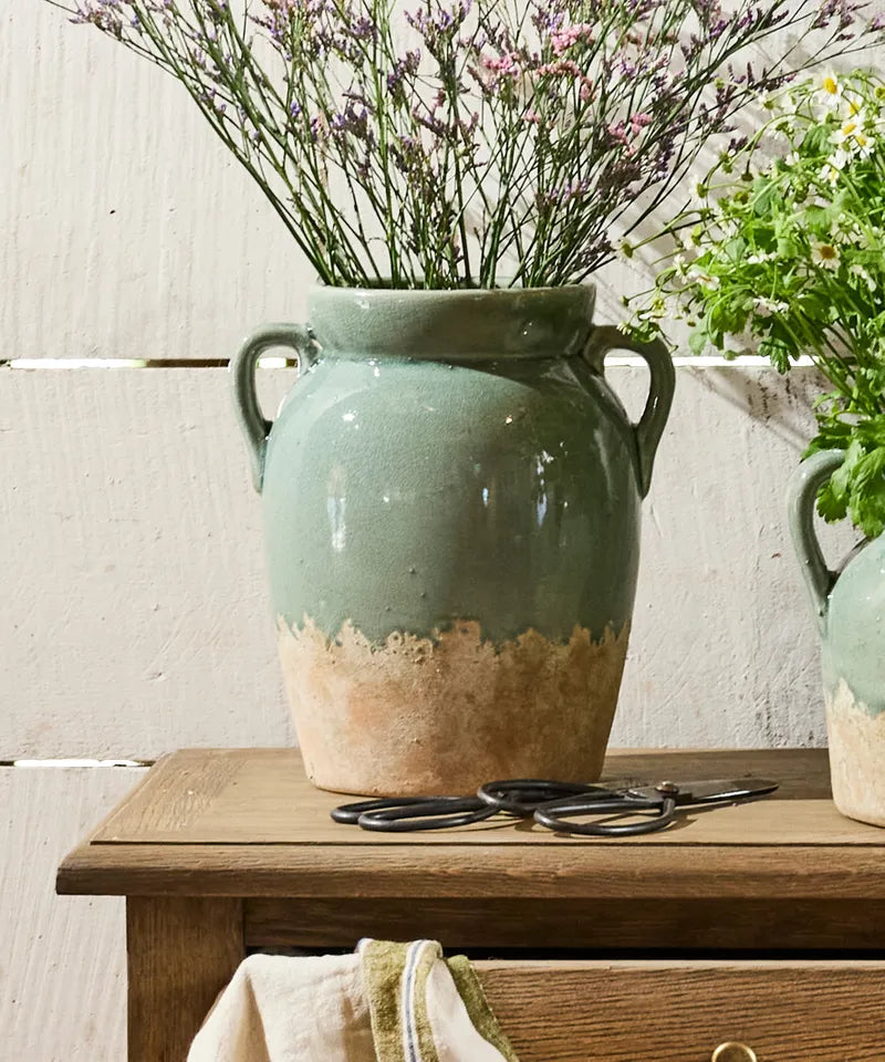 French Country Collections Varese Vessel Tall Pale Blue A handmade ceramic vase with two side handles, featuring a sage green glazed upper body and a rustic, unglazed terracotta-colored base